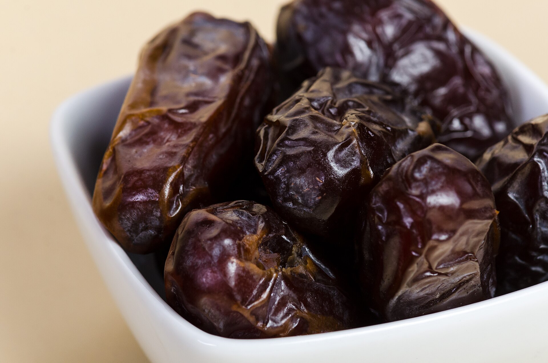 A white bowl of soft, glossy Medjool dates