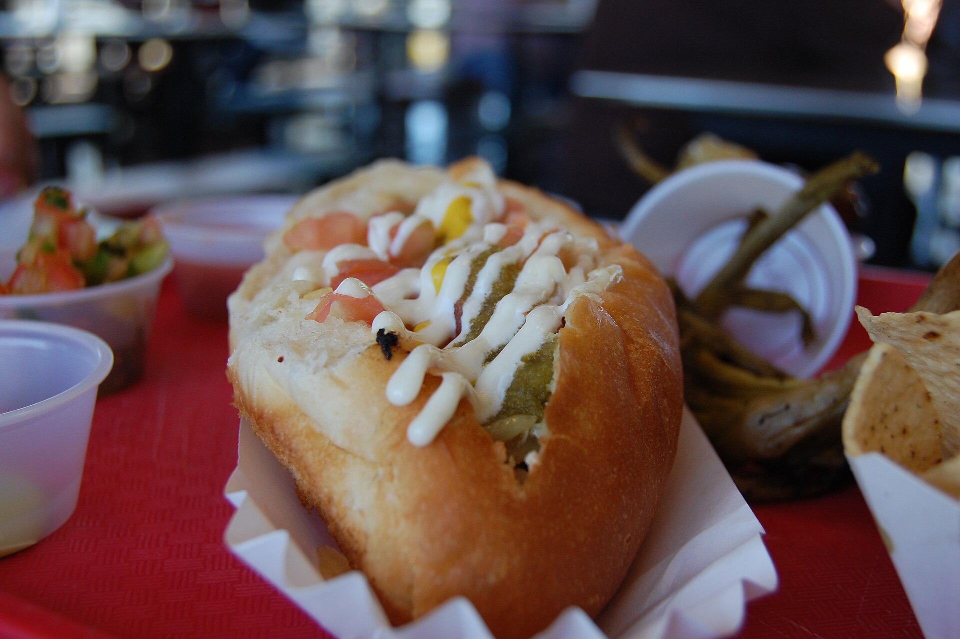 A Sonoran hot dog in a bolillo-style bun with beans, tomatoes, onions, mustard and mayonnaise